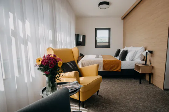 Prostorný apartmán se žlutým křeslem, květinami a velkoformátovým oknem